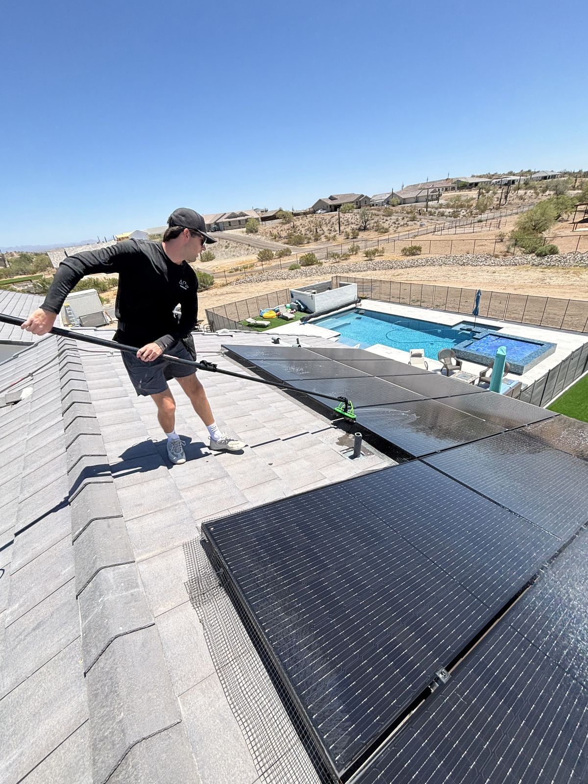 Apex Power Washing technician cleaning rooftop solar panels above a backyard pool